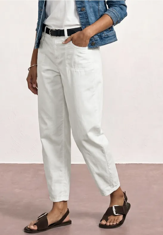 Weiße Bundfaltenhose mit schwarzem Gürtel, Jeansjacke, weißem Top und schwarzen Sandalen.