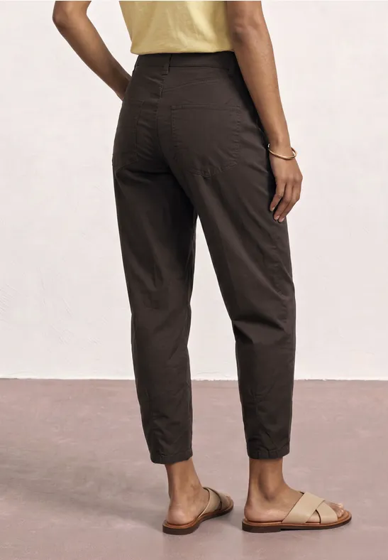 Achteraanzicht van een vrouw met bruine, enkellange broek en sandalen.