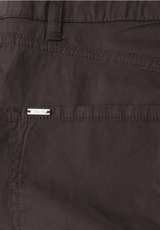 Close-up van een donkerbruine broek van stof met zak en klein metalen label.