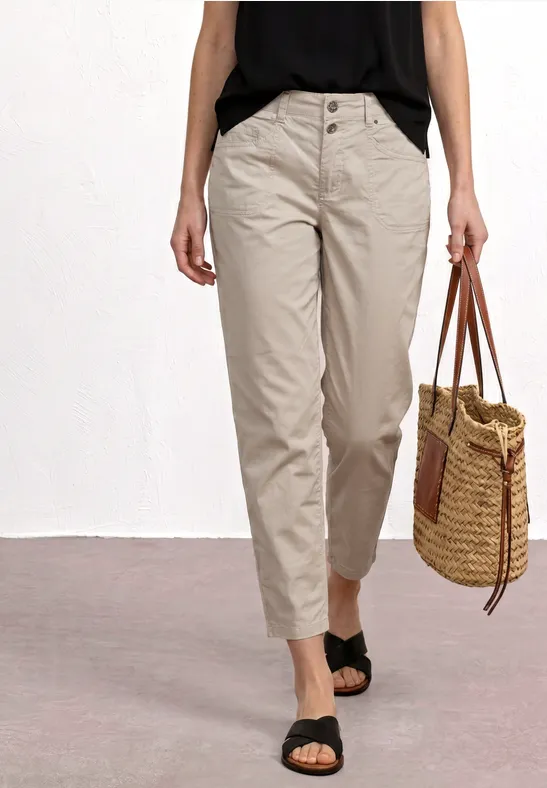 Femme portant un pantalon beige taille haute, top noir, sandales et un sac en osier tressé.