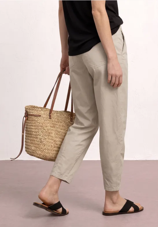 Personne porte un pantalon beige, des sandales noires et tient un panier tressé en paille.