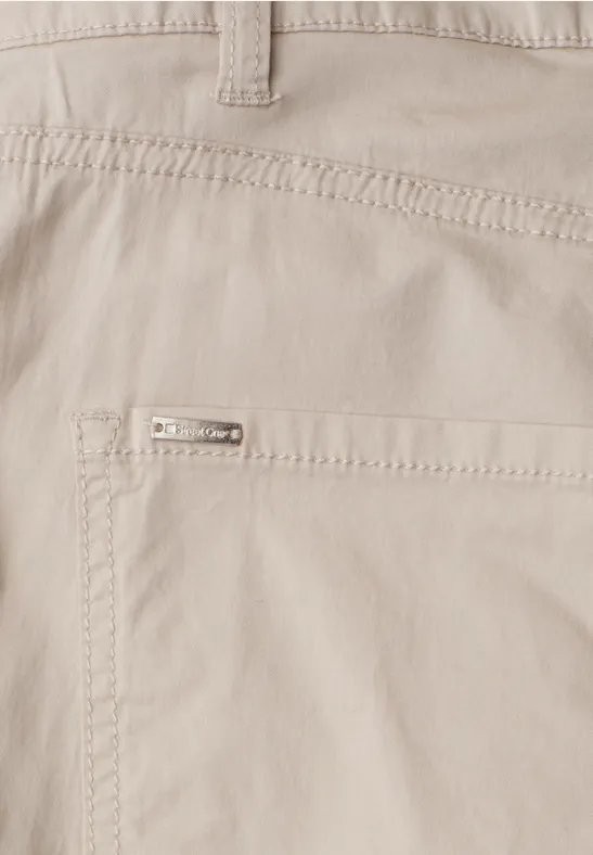 Gros plan sur un pantalon beige clair avec poche appliquée et petit logo métallique.