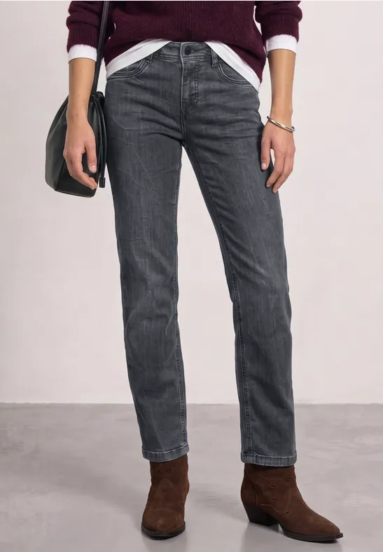 Une personne porte un jean gris foncé et des bottines marron avec un t-shirt blanc et un cardigan bordeaux.