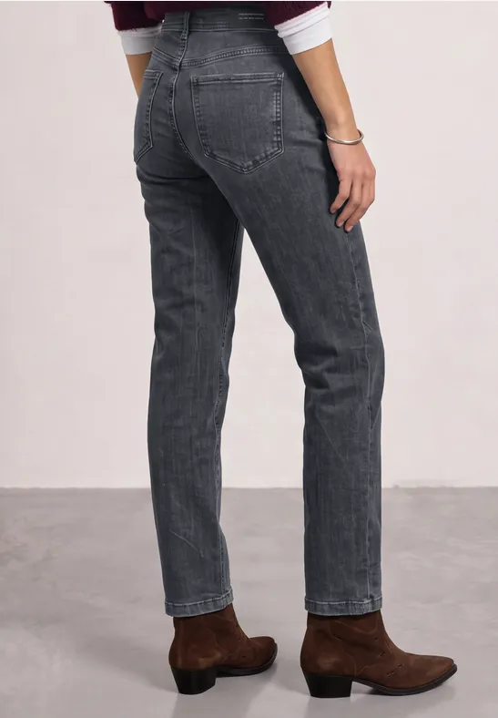 Personne portant un jean gris droit et des bottines marron sur un fond neutre.