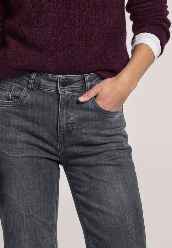 Vue partielle d’une personne en jean gris, pull violet et chemise blanche, main dans la poche.