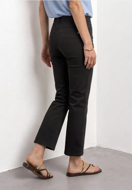 Vue latérale d'une personne portant un pantalon noir et des sandales marron devant un mur blanc.