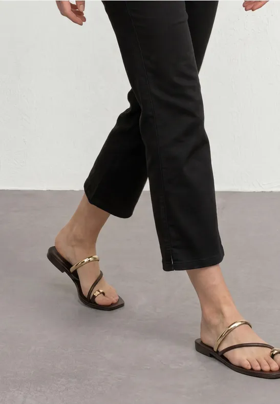 Jambes féminines avec pantalon noir et sandales plates à brides dorées