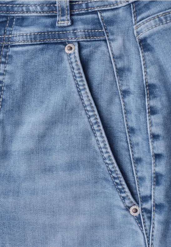 Detail einer hellblauen Jeanshose mit schräger Vordertasche und Metallnieten.