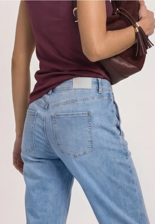 Rückansicht einer Person in hellblauen Jeans und burgunderrotem Top mit brauner Schultertasche.