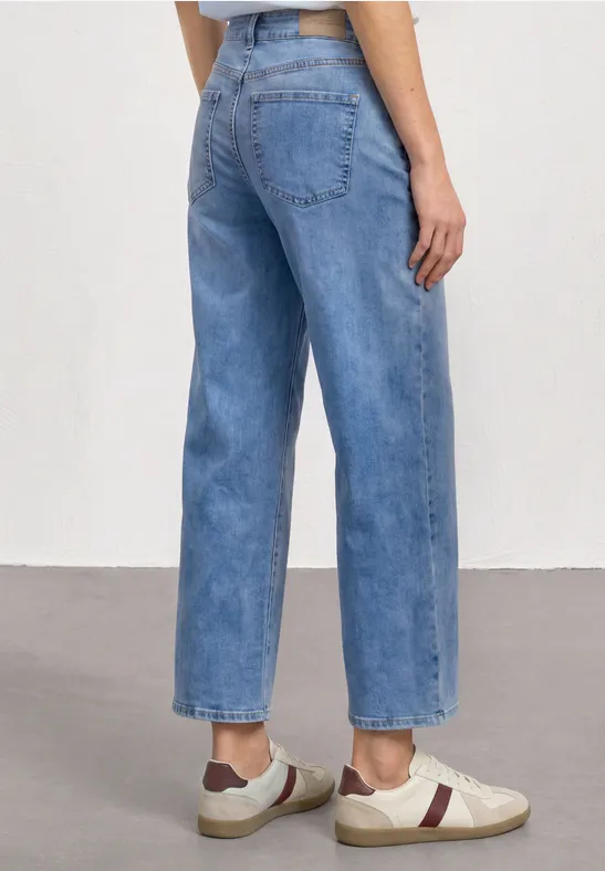 Vue arrière d'une personne en jean bleu clair droit et baskets blanches avec détails rouges.