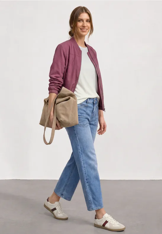 Femme en tenue décontractée: bomber bordeaux, t-shirt blanc, jeans droits, baskets blanches et sac en toile.
