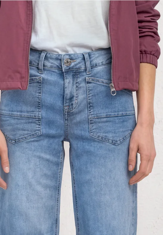 Personne porte un jean bleu clair, un t-shirt blanc et une veste rouge, buste et mains visibles.
