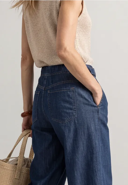 Femme de dos portant un jean large et un top beige, tenant un sac en paille.