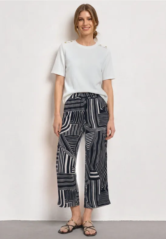 Femme portant un t-shirt blanc et un pantalon ample à motifs noirs et sandales