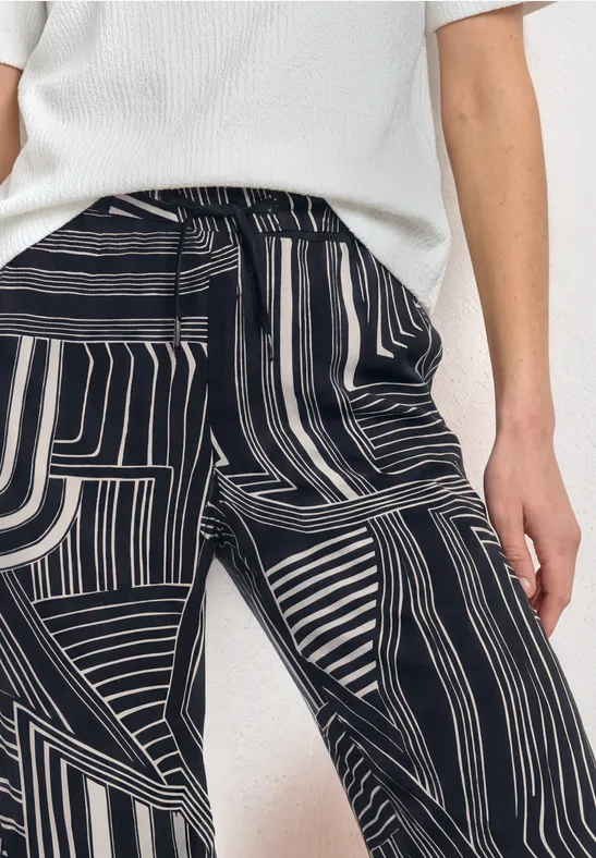 Personne portant un haut blanc et un pantalon noir et blanc à motif rayé abstrait.