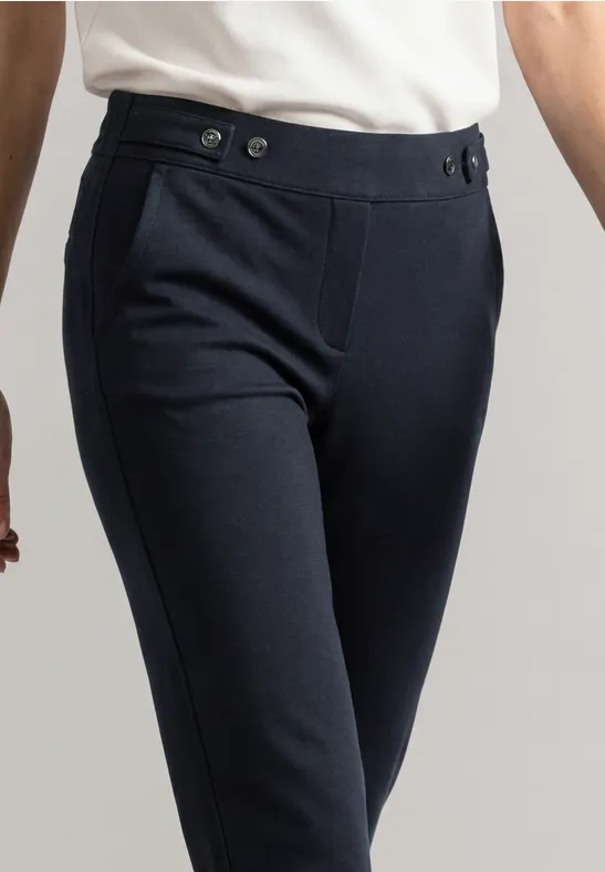Dunkelblaue, schmal geschnittene Hose mit Bundknöpfen, getragen mit weißem Oberteil.