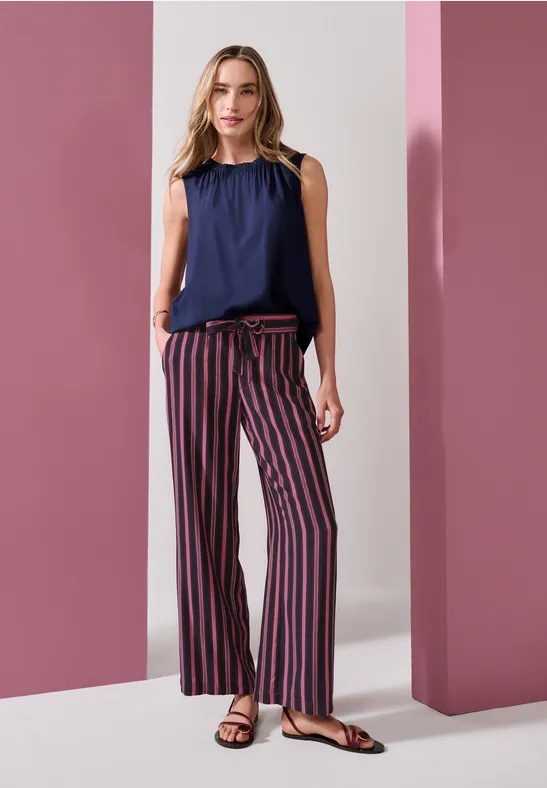 Vrouw in mouwloze donkerblauwe top en gestreepte wijde broek voor roze zuilen.