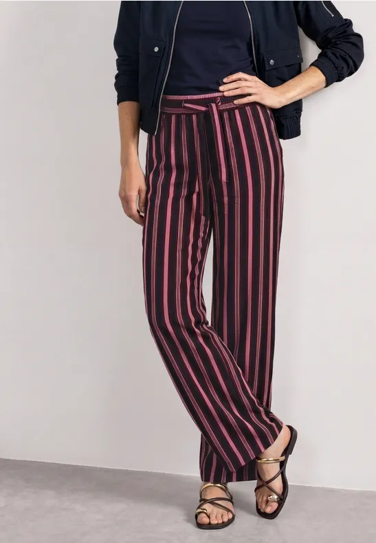Vrouw draagt een marineblauw jasje, t-shirt, wijde broek met rood-witte strepen en sandalen.