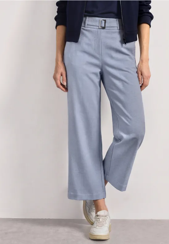Pantalon culotte bleu clair taille haute avec ceinture, porté avec baskets blanches.