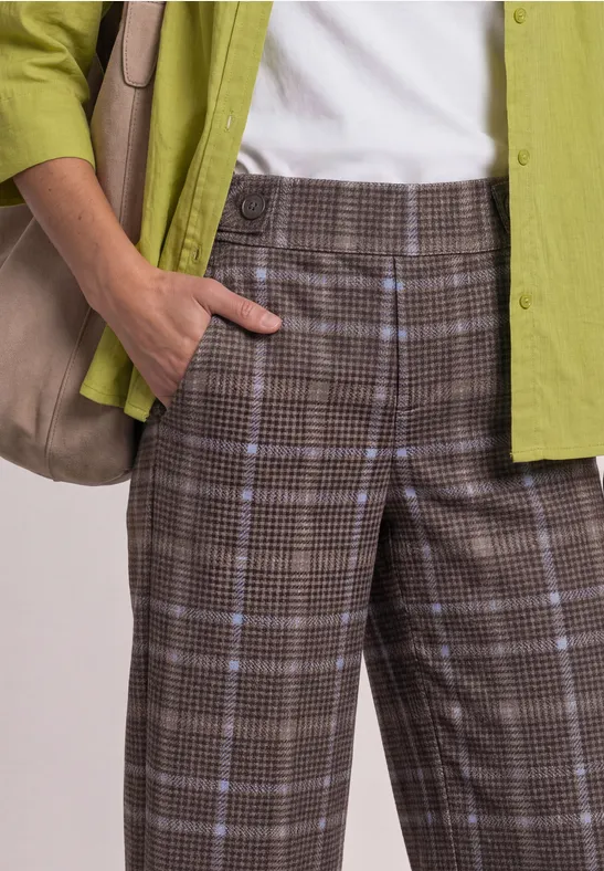 Personne porte un pantalon marron à carreaux, un top blanc, une chemise verte et un sac épaule.