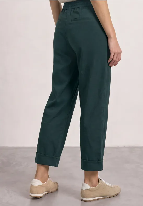Femme portant un pantalon taille haute gris foncé à revers et des baskets beiges.