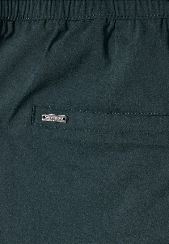 Gros plan d’un pantalon sombre avec poche zippée et petit logo métallique.