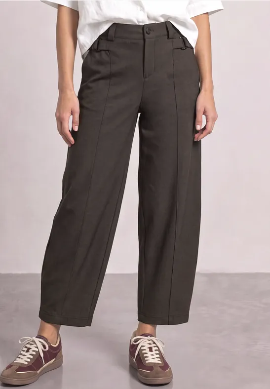 Femme portant un pantalon ample gris foncé taille haute, poches latérales et baskets décontractées.