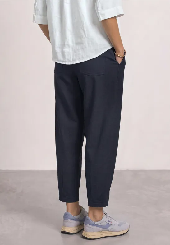 Personne vue de côté portant un pantalon bleu marine ample coupé aux chevilles, chemise blanche et baskets claires.