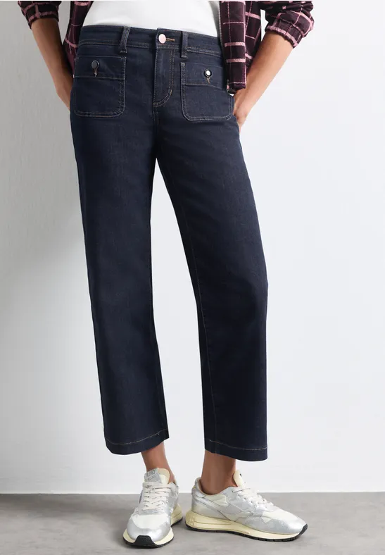 Donkerblauwe damesjeans met rechte pijpen tot op de enkels, gecombineerd met zilverkleurige sneakers.
