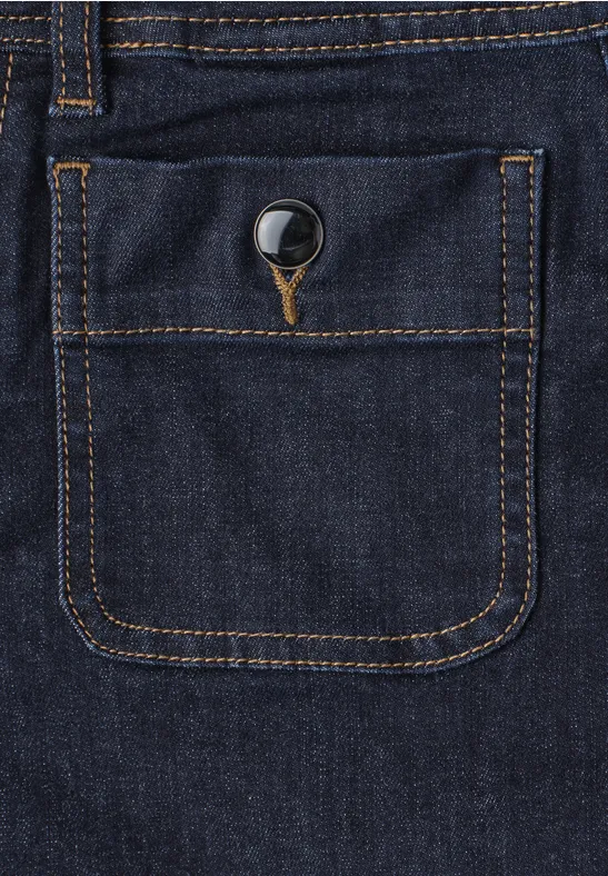 Close-up van een donkerblauwe spijkerbroekzak met metalen knoop en contrasterende stiksels