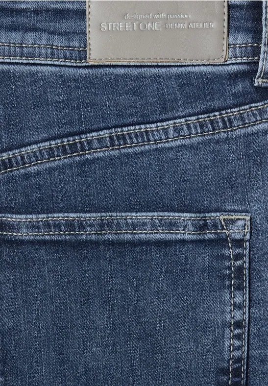 Nahaufnahme eines dunkelblauen Jeansstoffs mit zwei Taschen und Markenlabel am Bund.