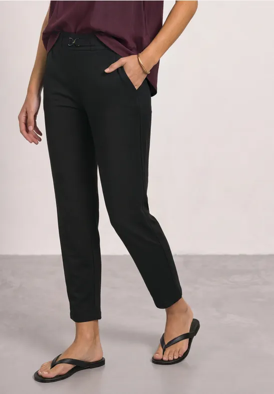Strakke zwarte enkellange broek met zijzakken, gecombineerd met zwarte teenslippers.