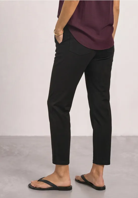 Een persoon draagt een paarse blouse, zwarte driekwartbroek en zwarte slippers.