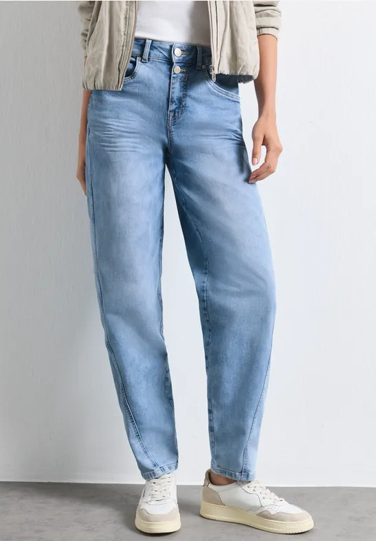 Une personne porte un jean ample bleu clair et des baskets blanches.