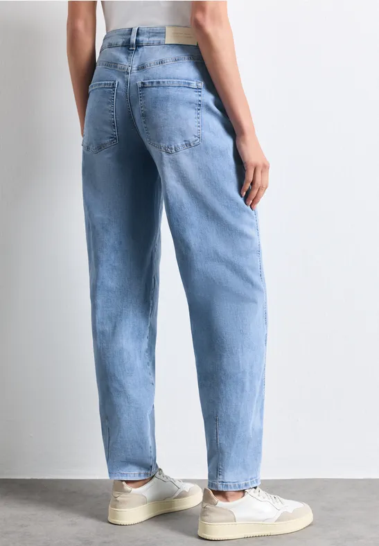 Personne vue de dos portant un jean bleu clair ample et des baskets beiges sur fond blanc.