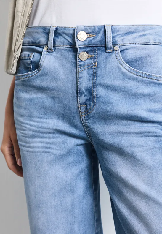 Gros plan d'un jean bleu clair avec bouton, braguette et poches apparentes.