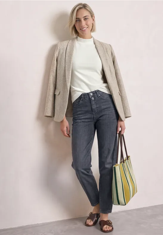 Femme en pull blanc, blazer beige, jean foncé, sandales et sac rayé sur fond neutre.
