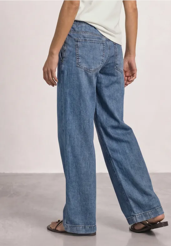 Person von hinten in weit geschnittenen blauen Jeans und Sandalen.