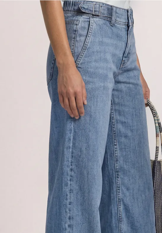 Frau trägt eine weit geschnittene blaue Jeans und hält eine geflochtene Tasche.