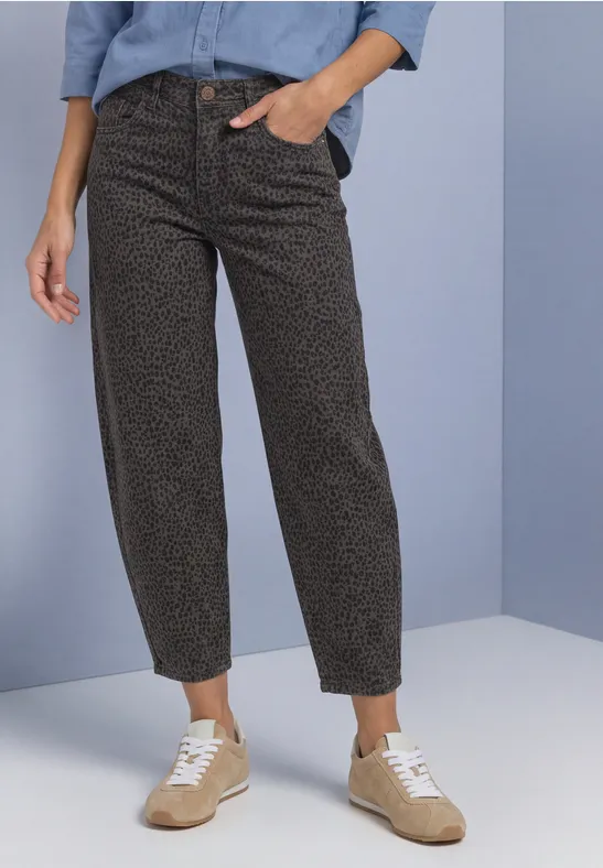 Personne porte un pantalon noir à motif et des baskets beiges devant un fond bicolore.