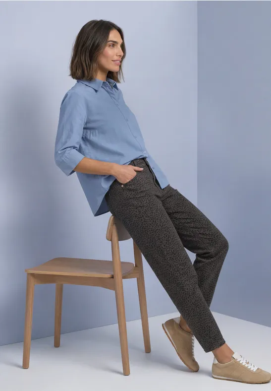Femme appuyée sur un tabouret, chemise bleu clair, pantalon foncé et baskets beiges.