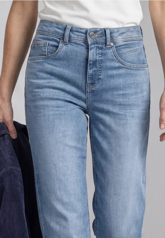 Jean en denim bleu clair taille haute, coupe ajustée, poches avant, une veste bleu foncé tenue à la main.