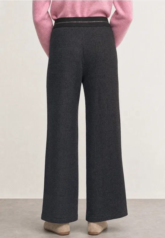 Achteraanzicht van een persoon in hoge, wijdvallende donkergrijze broek en beige hakken.