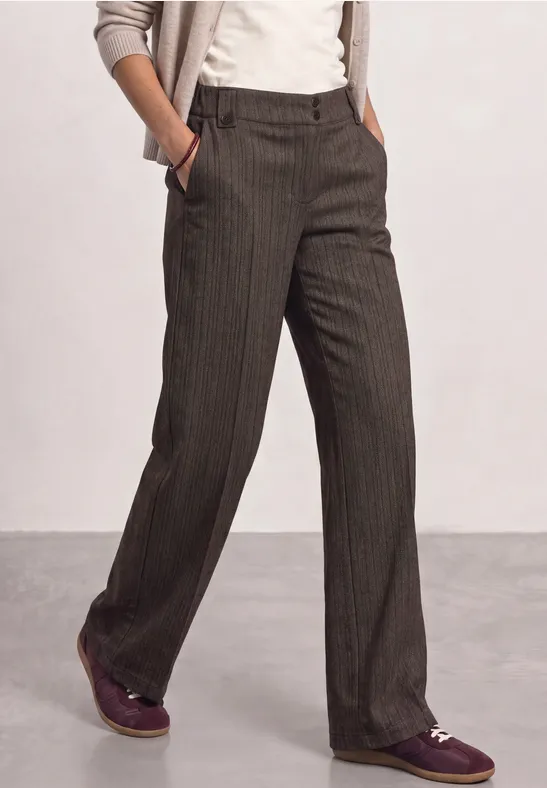 Person trägt graue, gestreifte Hose, weißes Shirt, beigefarbener Cardigan und lila Schuhe.