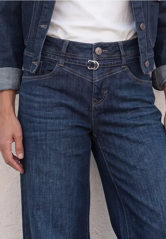 Une personne porte un jean bleu et une veste en jean, taille marquée par une boucle de ceinture stylée.