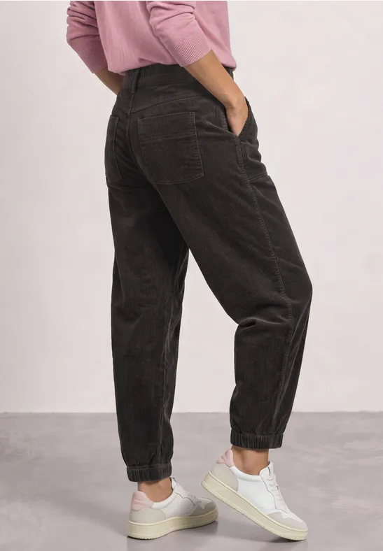 Vue latérale d'une personne portant un pantalon ample noir, un pull rose et des baskets blanches.