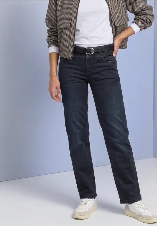 Iemand draagt rechte donkerblauwe jeans, witte sneakers, een zwarte riem en een licht overhemd.