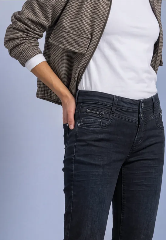 Iemand draagt een wit T-shirt, een olijfgroene jas en donkere jeans, de hand in de zak.