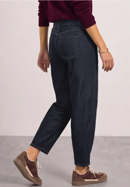 Personne de profil en jean bleu foncé, baskets marron et pull bordeaux.