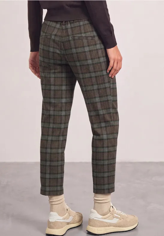 Rugaanzicht van een persoon met groengrijs geruite broek en beige sneakers.